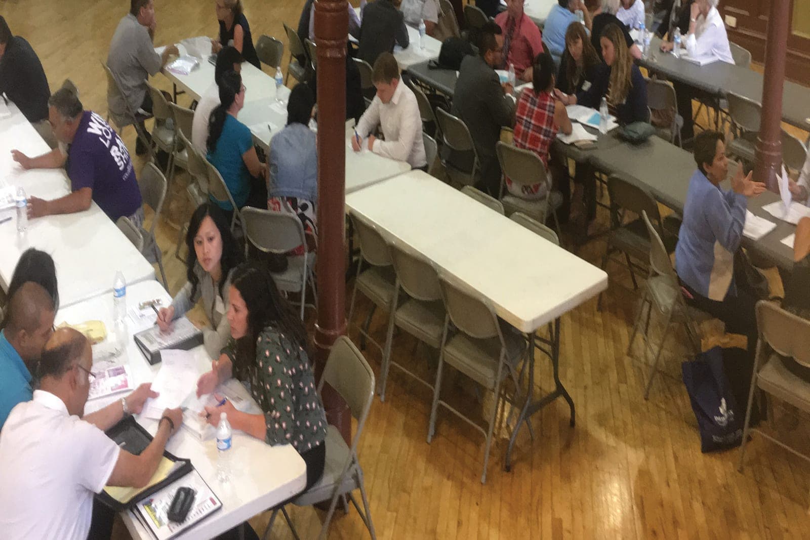 Volunteer lawyers meeting with clients at long folding tables in a busy clinic hall